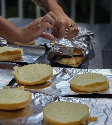About Us Person wrapping burger buns in foil, ideal for outdoor grilling or picnic.